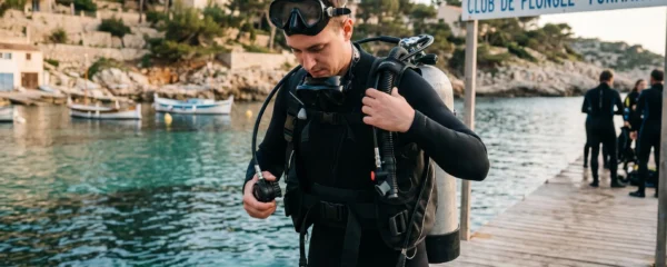 Plongeur débutant en combinaison néoprène portant un gilet stabilisateur avec bouteille, ajustant les sangles du gilet au bord d'un bassin de formation ou d'une crique méditerranéenne